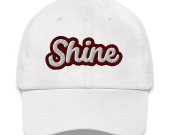 May include: White baseball cap with a red and white embroidered word "Shine" on the front.