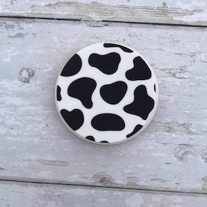 May include: A round white cookie with a black and white cow print design.
