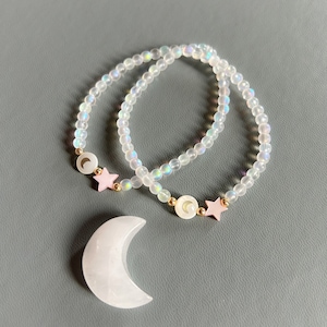 May include: Two iridescent white beaded bracelets with pink star and crescent moon charms. A larger white crescent moon charm is also included.