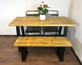 May include: A wooden table with a black metal base and a matching wooden bench. The table is set with two black chairs and a white planter with a red flower.