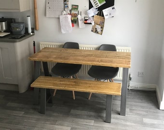 May include: A wooden dining table with a rustic finish and black metal legs. The table is paired with a matching wooden bench and two black chairs.