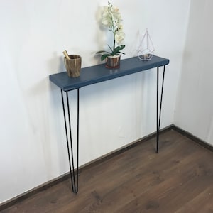 May include: A dark blue console table with a wooden top and black hairpin legs. The table is decorated with a small potted plant, a wooden bowl, and a geometric metal ornament.
