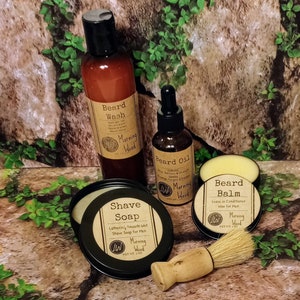 May include: A set of beard care products in a woodsy setting. The set includes a beard wash, beard oil, beard balm, and shave soap. All products are labeled with the scent "Morning Wood".