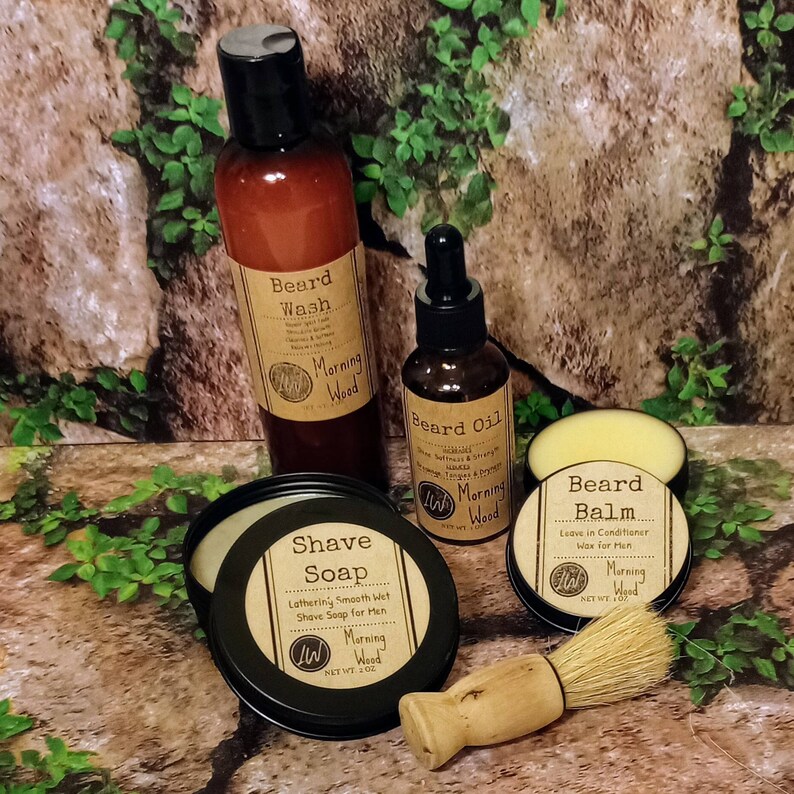 May include: A set of beard care products in a woodsy setting. The set includes a beard wash, beard oil, beard balm, and shave soap. All products are labeled with the scent "Morning Wood".