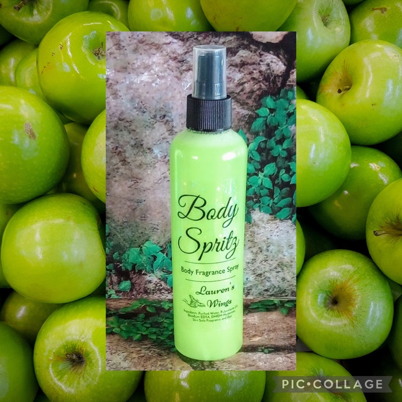K&ouml;nnte beinhalten: Eine gr&uuml;ne Glasflasche mit schwarzem Spr&uuml;hkopf. Die Flasche ist mit "Body Spritz" und "Lauren's Wings" sowie einem gr&uuml;nen Blattdesign beschriftet. Die Flasche ist von gr&uuml;nen &Auml;pfeln umgeben.
