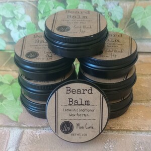 May include: A stack of eight small black tins with brown labels. The labels read "Beard Balm", "Leave in Conditioner Wax for Men", "Man Cave", "Net Wt. 1 oz", and "Solid Black Ice".