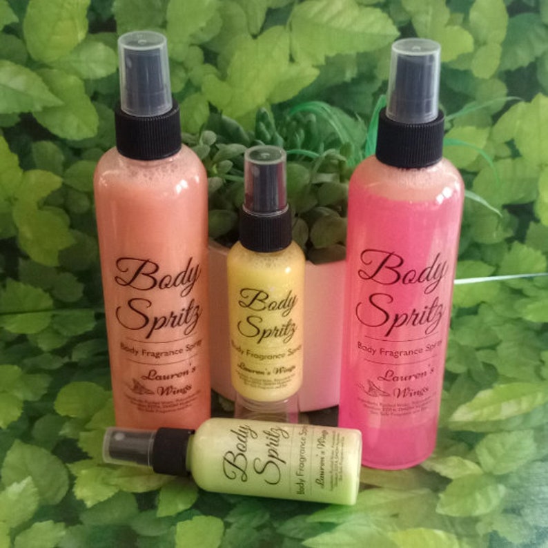 K&ouml;nnte beinhalten: Drei Flaschen K&ouml;rperspray in Pink, Gelb und Gr&uuml;n. Die Flaschen sind mit "Body Spritz" und "Body Fragrance Spray" beschriftet. Der Text auf den Flaschen lautet auch "Lauren's Wings".