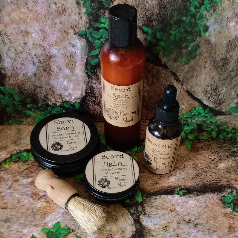 May include: A set of beard care products in a woodsy setting. The set includes a beard wash, beard oil, beard balm, and a shave soap. All products are labeled with the scent "Morning Wood".