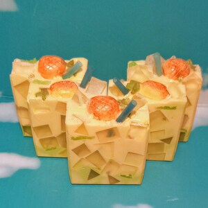 May include: Four square bars of soap shaped like a glass of iced tea with a straw and a pineapple slice on top. The soap is a light yellow color with green and clear accents.