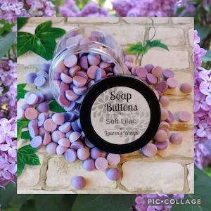 May include: A glass jar filled with purple and white soap buttons labeled "Soap Buttons Soft Lilac Lauren's Wings".