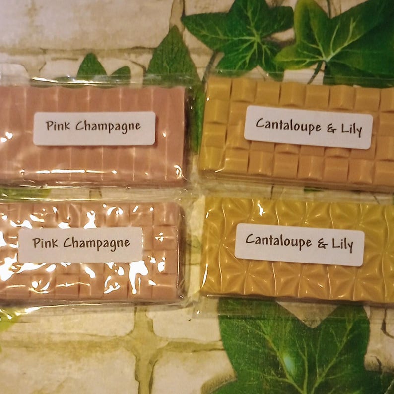 May include: Four wax melts, two pink and two yellow, with labels. The pink melts are labeled "Pink Champagne" and the yellow melts are labeled "Cantaloupe & Lily".