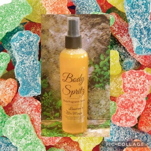 May include: A clear glass bottle with a yellow liquid inside. The bottle has a black spray nozzle and a white label that says "Body Spritz Body Fragrance Spray Lauren's Wings". The bottle is surrounded by colorful gummy candies.