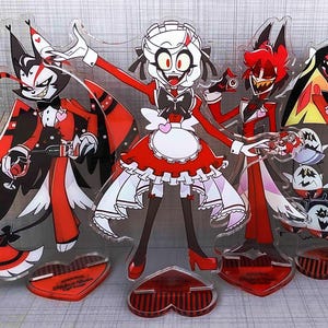 Może przedstawiać: Akrylowe stojaki z postaciami z kreskówek w kolorze czerwonym, czarnym i białym. Postacie mają przesadzone cechy i pozują w różnych pozach. Każdy stojak ma podstawę w kształcie serca.