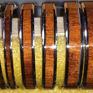 May include: A collection of six rings with a polished silver band and a textured, reddish-brown wood inlay. The rings are displayed on a yellow surface, showcasing their contrasting materials and design.
