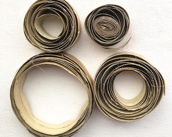 May include: Four rolls of brown paper tape, each rolled into a circle, are arranged on a white surface. The rolls are different sizes, with the largest roll in the center of the image.