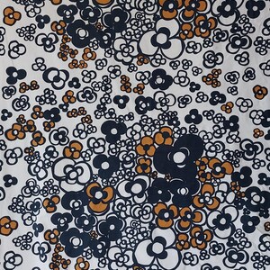 May include: White fabric with a repeating floral pattern in navy blue, orange, and white. The flowers are stylized and clustered together. The fabric is likely used for clothing or home decor.