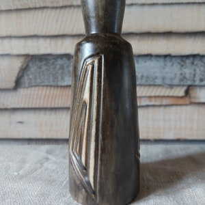 Puede incluir: Un jarrón de cerámica marrón oscuro con un diseño geométrico en blanco. El jarrón tiene un cuello estrecho y una base ancha.