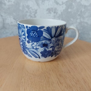 May include: A white ceramic teacup with a blue floral pattern. The cup has a rounded shape and a handle.