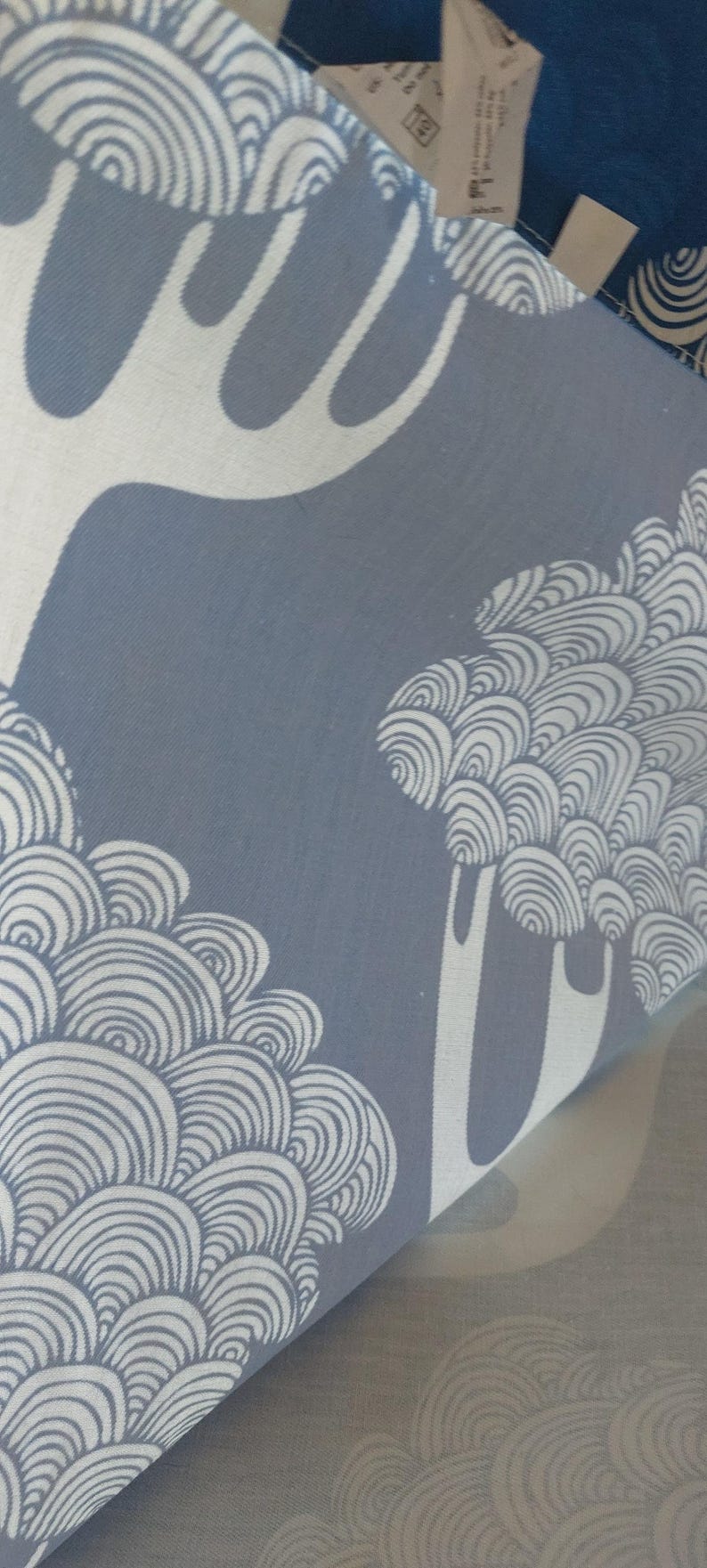 Puede incluir: Primer plano de una tela estampada azul y blanca. El dise&ntilde;o presenta formas estilizadas de &aacute;rboles y patrones arremolinados. La tela est&aacute; doblada, revelando la repetici&oacute;n del patr&oacute;n.