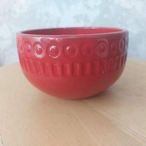 May include: A red ceramic bowl with a decorative pattern of circles and lines around the rim.
