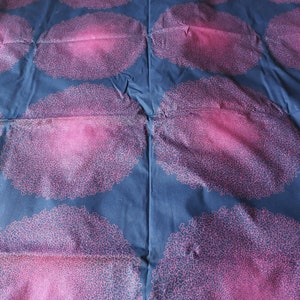May include: A dark blue fabric with a repeating pattern of pink, circular designs. The designs are made up of a series of small, intricate lines.