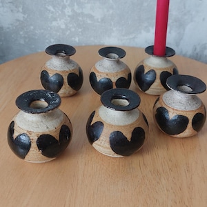 May include: Set of seven ceramic candle holders with black heart designs. The holders are beige with a brown glaze. One holder has a red candle.