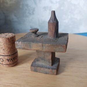 May include: A miniature wooden table with a single leg and a small wooden bottle and a wooden cup on top.