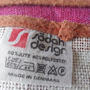 May include: A white label with black text that reads "r&ouml;dah design" and "60% JUTE 40% POLYESTER". The label also includes care instructions and the text "MADE IN DENMARK".