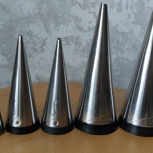 May include: Five silver metal piping tips of varying sizes, with black plastic bases. The tips are arranged in order of size, from smallest to largest.