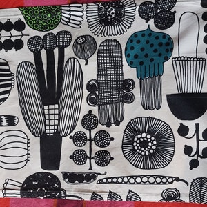 May include: A white tea towel with a black and green floral pattern. The pattern features stylized flowers, leaves, and stems.