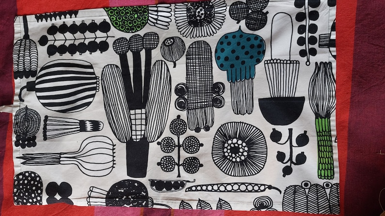 May include: A white tea towel with a black and green floral pattern. The pattern features stylized flowers, leaves, and stems.