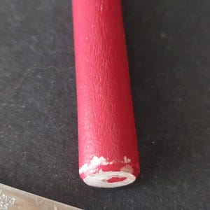 May include: Close-up of a spoon with a red handle and a silver blade. The red paint on the handle is chipped, revealing the wood underneath. Another spoon with a black handle is partially visible.