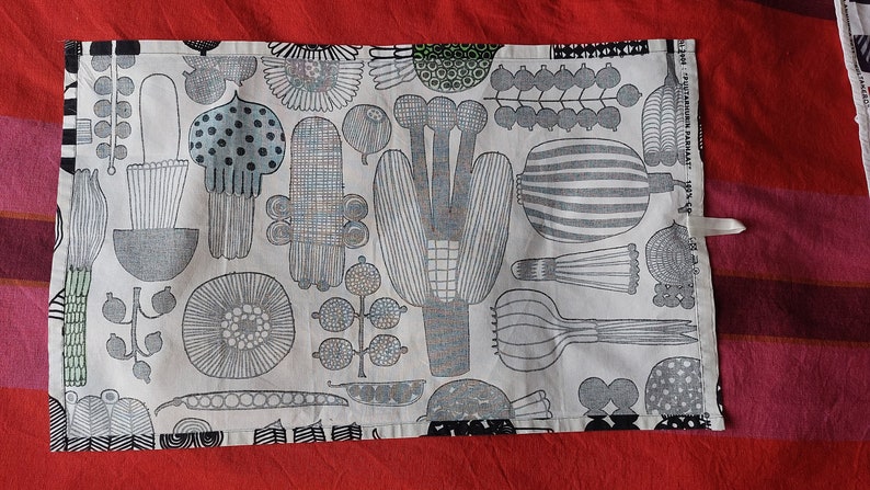 May include: A white tea towel with a black and gray pattern of stylized plants and flowers. The towel has a loop for hanging.