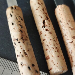 May include: Close-up of three cork-handled tools with metal blades. The cork handles are cylindrical, light brown, and speckled with dark spots. A metal ruler with inch markings is in the foreground, indicating the size of the tools.