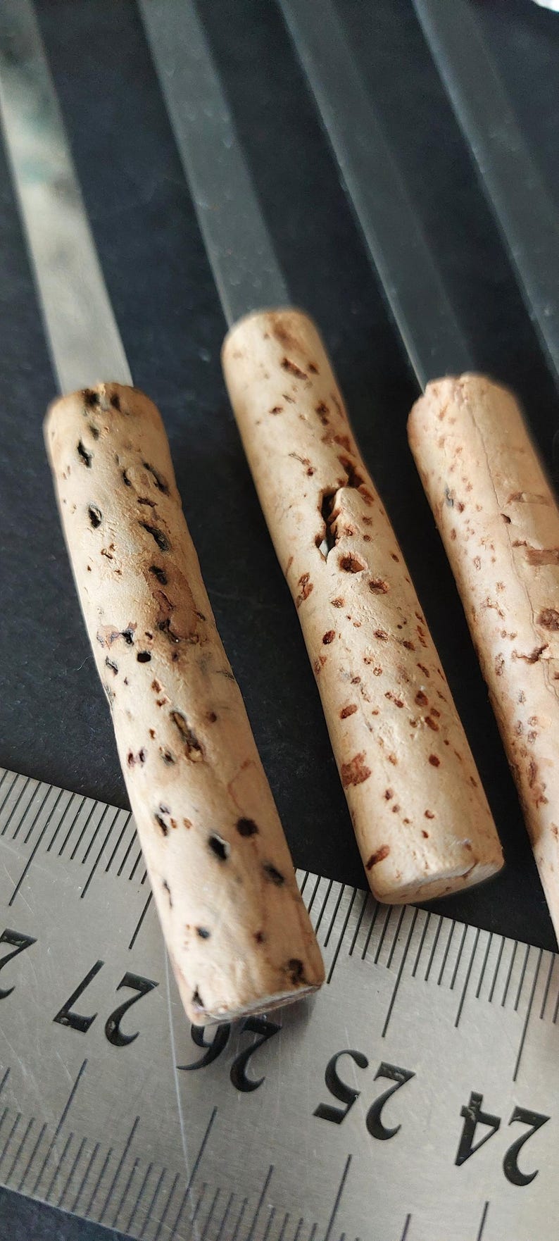 May include: Close-up of three cork-handled tools with metal blades. The cork handles are cylindrical, light brown, and speckled with dark spots. A metal ruler with inch markings is in the foreground, indicating the size of the tools.