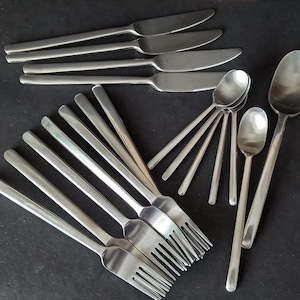 May include: A selection of stainless steel cutlery, comprising knives, forks, and spoons, displayed on a dark background. The set features different spoon and fork sizes, with a total of 20 items. The cutlery has a minimalist, contemporary aesthetic.