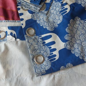 Puede incluir: Cortinas estampadas en azul y blanco con ojales plateados. Las cortinas presentan un dise&ntilde;o repetitivo de formas estilizadas en forma de nube. El fondo es una mezcla de rojo, rosa y morado.
