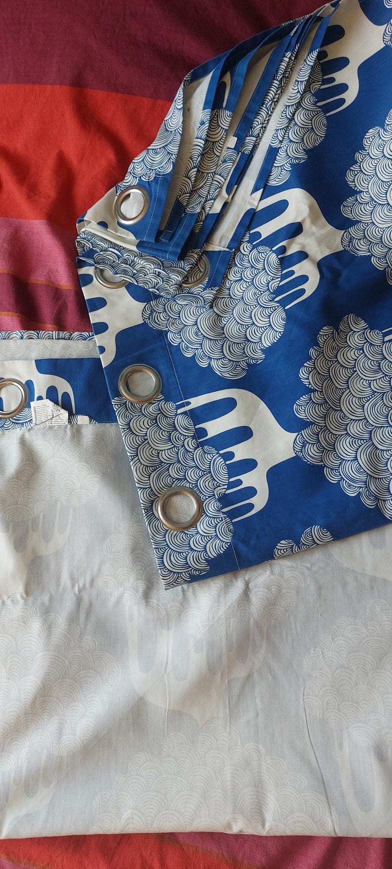 Puede incluir: Cortinas estampadas en azul y blanco con ojales plateados. Las cortinas presentan un dise&ntilde;o repetitivo de formas estilizadas en forma de nube. El fondo es una mezcla de rojo, rosa y morado.