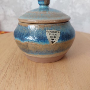 Könnte beinhalten: Eine blaue und braune Keramikdose mit Deckel. Die Dose trägt ein Etikett mit der Aufschrift "M/R ANDERSEN & SBN BORNHOLMSK KERAMIK".