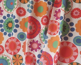 Puede incluir: Cortina blanca con un patrón repetitivo de flores estilizadas y lunares coloridos. Las flores son en tonos de rojo, naranja, rosa, verde y azul. La cortina está colgada, con pliegues visibles.