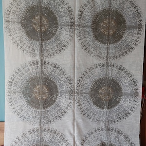 Könnte beinhalten: Weißer Stoff mit einem sich wiederholenden Muster aus vier großen, konzentrischen Kreisen in einem Grau- und Braunton. Die Kreise bestehen aus einer Reihe kleiner, sich wiederholender Symbole.