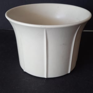 May include: A solid off-white planter with a smooth, matte finish and a wide, flared rim. The exterior features evenly spaced vertical ridges that extend from the base toward the top, creating a structured, clean, and simple cylindrical shape.
