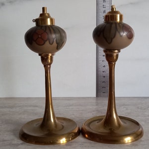 Può includere: Due lampade ad olio antiche in ottone con disegni floreali sui globi di vetro. Le lampade sono su una superficie bianca.