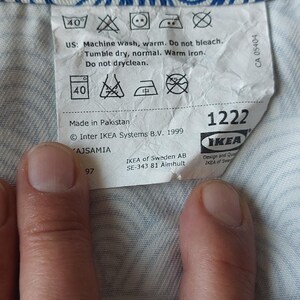 Puede incluir: Primer plano de una etiqueta blanca con instrucciones de lavado y el logotipo de IKEA. La etiqueta est&aacute; sobre una tela estampada azul y blanca. La etiqueta incluye el texto "Lavar a m&aacute;quina, caliente. No usar lej&iacute;a. Secar en secadora, normal. Planchar con plancha tibia. No limpiar en seco."
