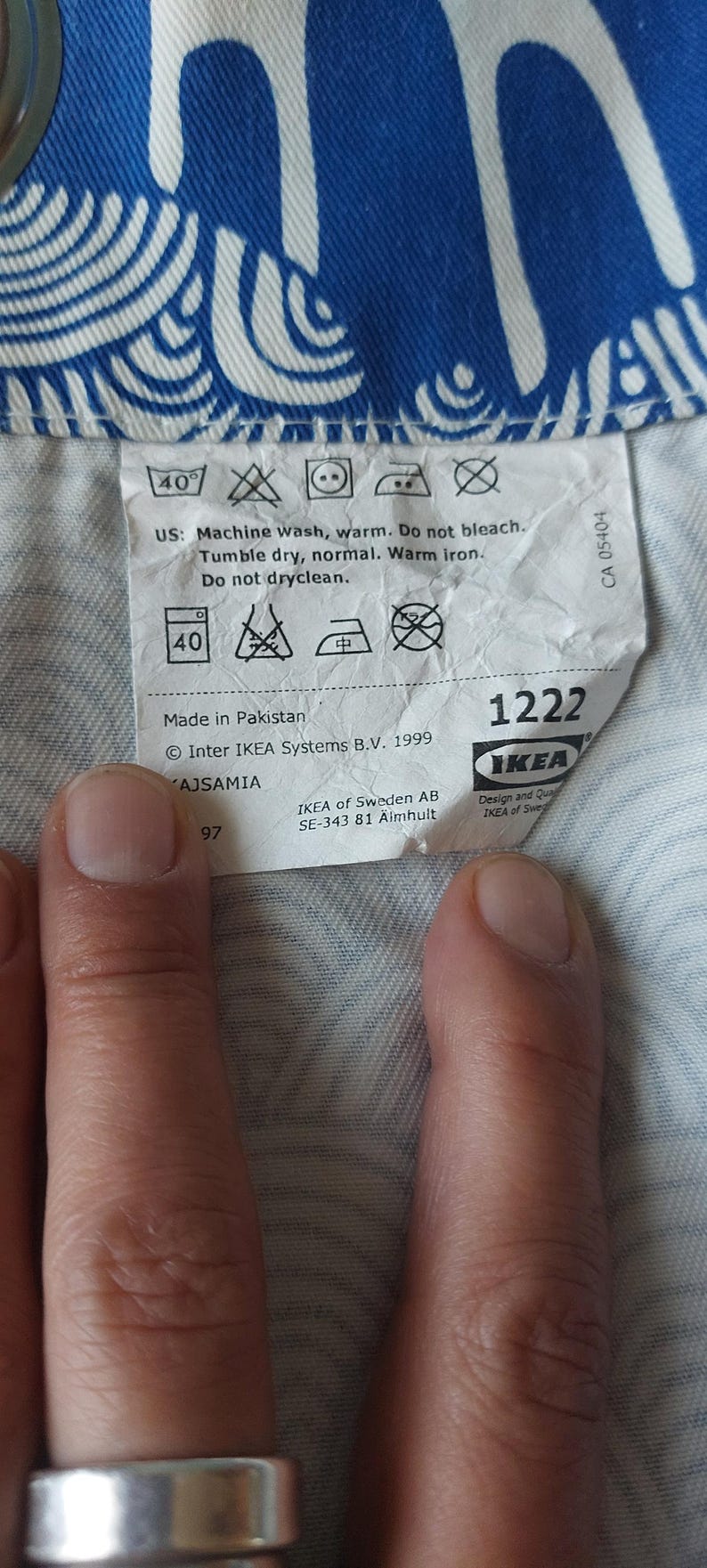 Puede incluir: Primer plano de una etiqueta blanca con instrucciones de lavado y el logotipo de IKEA. La etiqueta est&aacute; sobre una tela estampada azul y blanca. La etiqueta incluye el texto "Lavar a m&aacute;quina, caliente. No usar lej&iacute;a. Secar en secadora, normal. Planchar con plancha tibia. No limpiar en seco."
