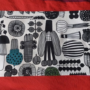 May include: A white kitchen towel with a black and white patterned design featuring various shapes, including mushrooms, flowers, and geometric patterns. The design also includes green accents.
