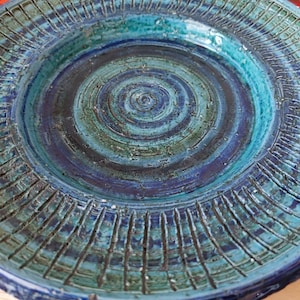Puede incluir: Un plato de cerámica azul y verde con un diseño de círculos concéntricos. El plato tiene un borde texturizado con líneas verticales.