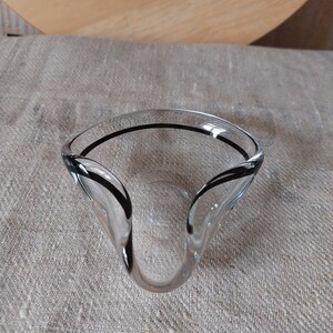 Könnte beinhalten: Eine klare Glasschüssel mit schwarzem Rand. Die Schüssel hat eine einzigartige, wellenförmige Form.