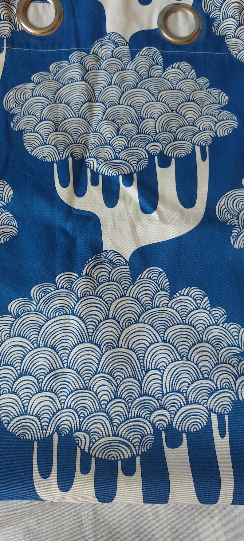 Puede incluir: Panel de cortina con estampado azul y blanco. El dise&ntilde;o presenta &aacute;rboles blancos estilizados con copas redondeadas y en capas sobre un fondo azul liso. La cortina tiene ojales met&aacute;licos en la parte superior para colgar.
