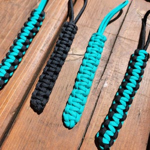 May include: Four handmade paracord keychains in black and turquoise. The keychains are made with a cobra stitch and have a loop at the top for attaching keys.